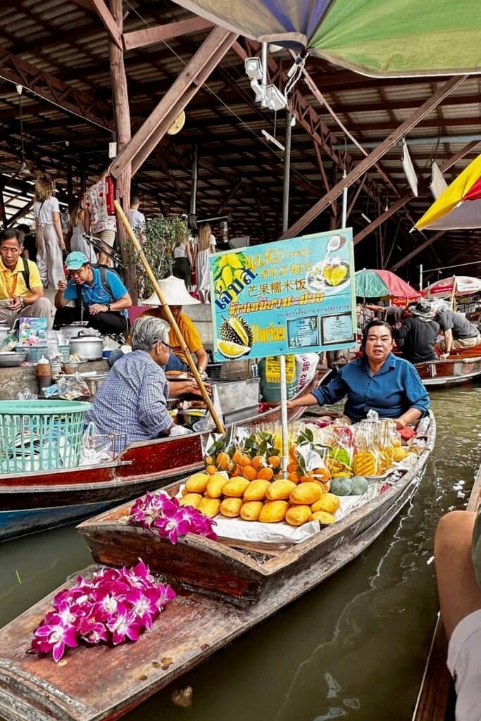 Damnoen Saduak’ta teknede mango sticky rice ve atıştırmalıklar satan satıcı, yüzen pazar manzarası.
