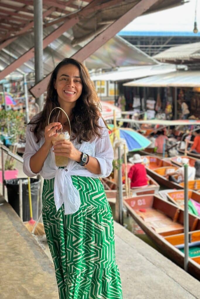 Damnoen Saduak Floating Market’te tekneler arasında içeceğini tutan gezgin, Tayland yüzen pazar atmosferi.