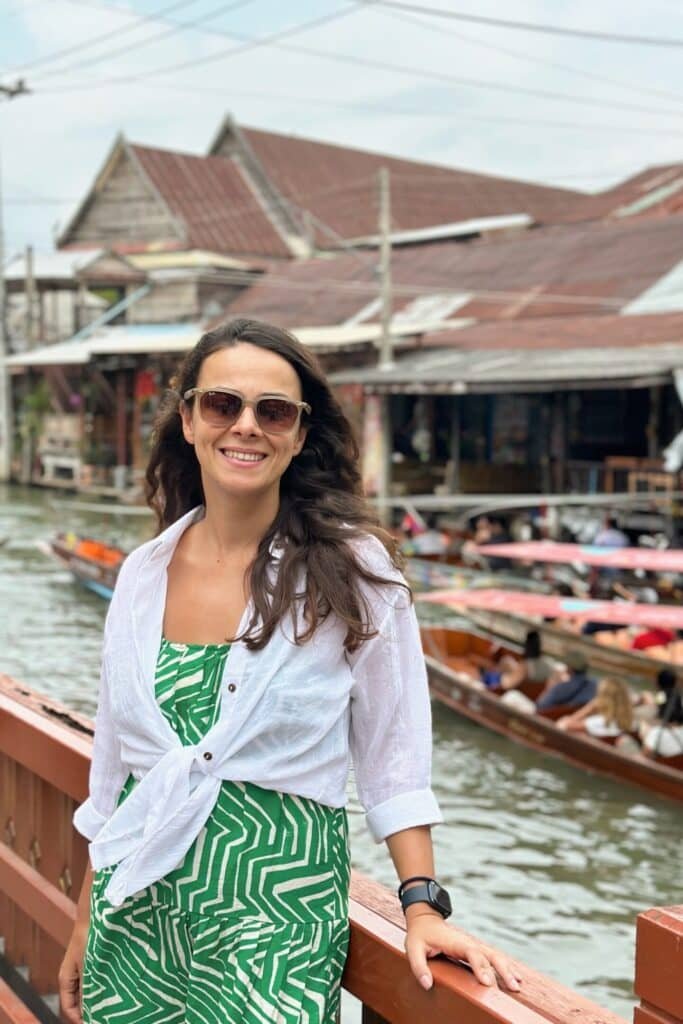 Damnoen Saduak’ta köprü üzerinde kanala karşı poz: arkada geçen tekneler ve yüzen pazar görüntüsü.