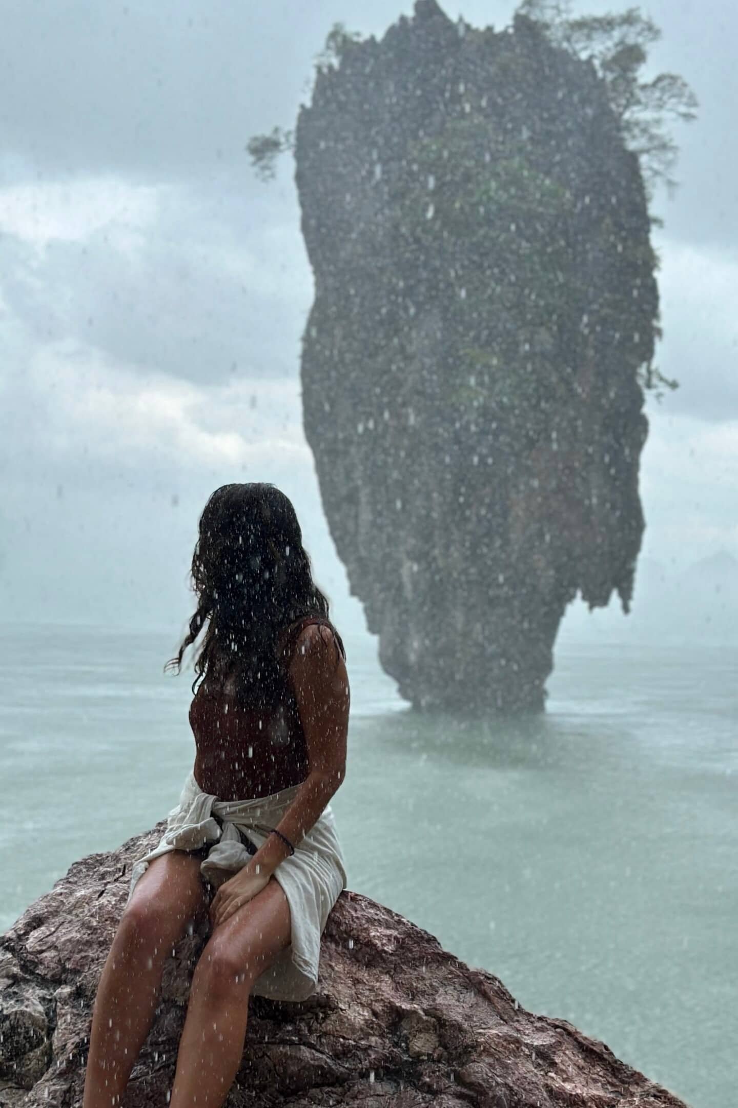 Yağmur altında kayada oturan kadın ve arkada Ko Tapu (James Bond Island)