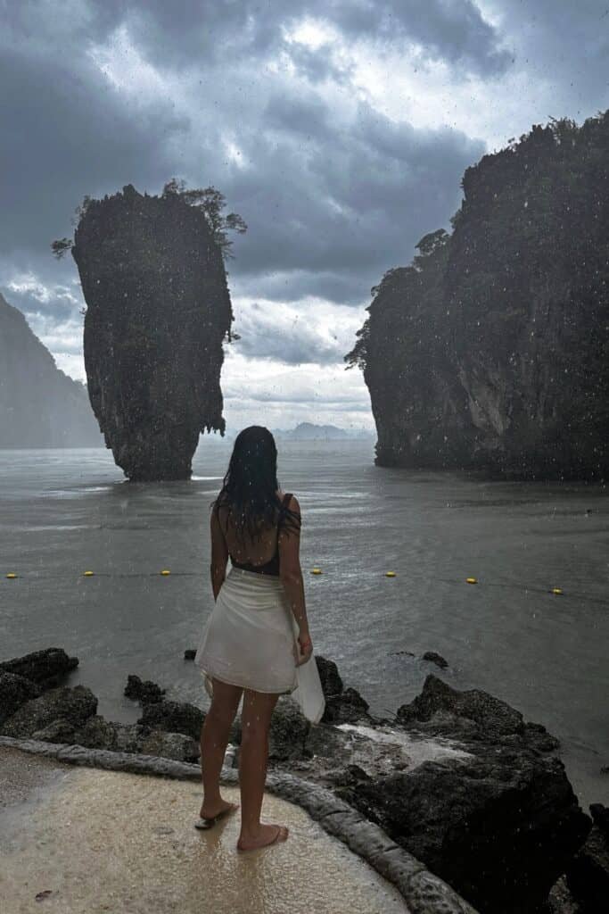 Fırtınalı havada sahilde duran kadın ve James Bond Island (Ko Tapu) silueti