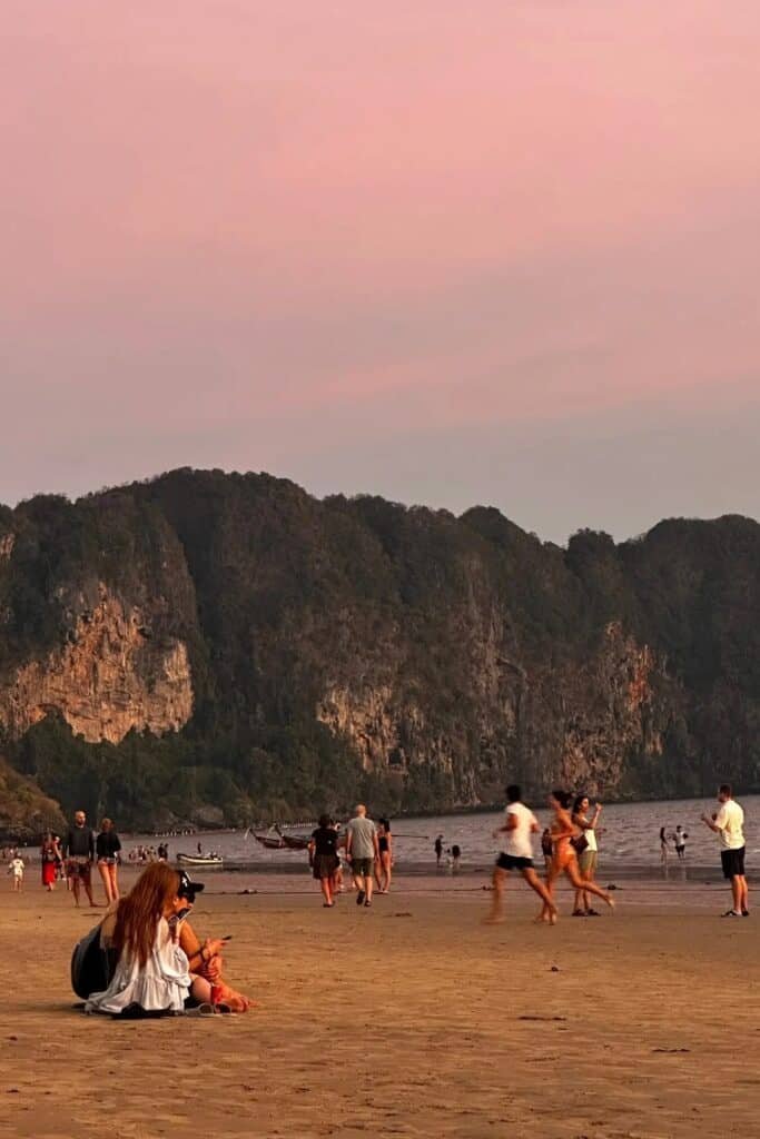 Krabi sahilinde gün batımı saatlerinde plajda yürüyen insanlar ve arka planda kayalık dağ manzarası