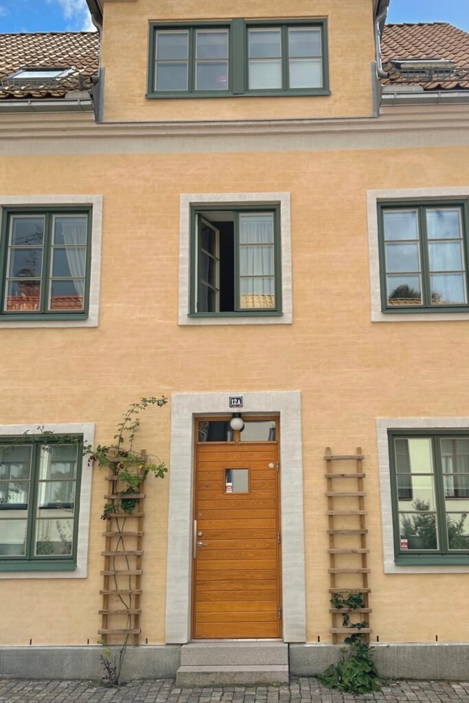 Lund eski şehirde pastel sarı cepheli, yeşil çerçeveli pencereli geleneksel İsveç evi, Lund’da 1 günde gezilecek yerler için fotojenik sokak detayı.