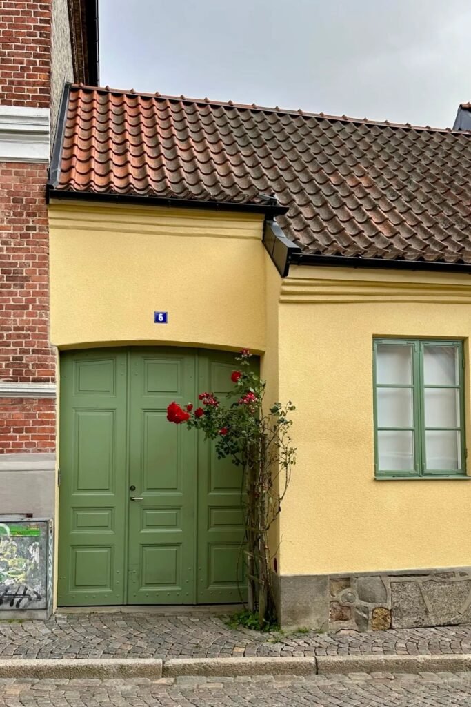 Lund sokaklarında sarı duvarlı küçük ev, yeşil çift kapı ve kırmızı güller, Lund seyahat rehberi için en güzel fotoğraf noktalarından biri.