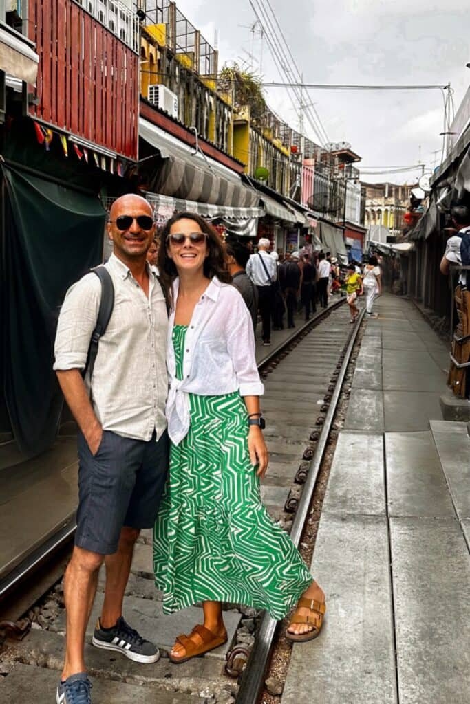 Maeklong Railway Market’te rayların üzerinde poz veren çift: Tayland tren pazarı sokak manzarası.