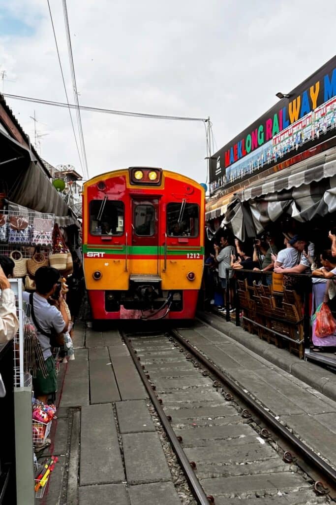 Maeklong Railway Market’te rayların arasından yaklaşan tren ve pazar tezgahları, Tayland’ın ünlü tren pazarı.
