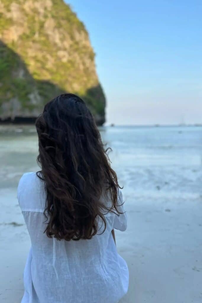 Phi Phi Maya Bay’de beyaz kumsalda oturup denizi izleyen kişi ve arka planda kayalıklar, maya bay hakkında bilmeniz gerekenler