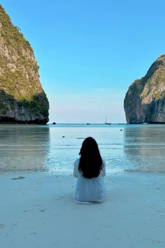 Phi Phi Maya Bay’de beyaz kumsalda oturup turkuaz denizi izleyen kişi ve kayalık manzara