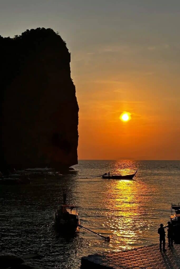 Phi Phi’de gün batımında deniz üzerinde longtail boat teknesi ve kayalık silüeti, Tayland