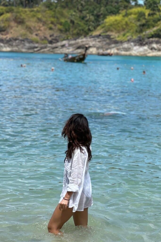 Phuket’te sığ denizde yürüyen kişi, arkada longtail tekne ve koy manzarası