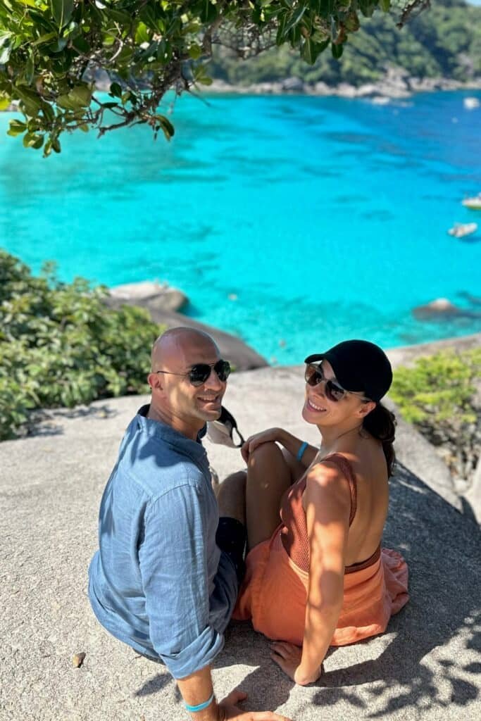 Similan Adaları’nda kayalıkta oturan çift, arkada turkuaz koy manzarası.