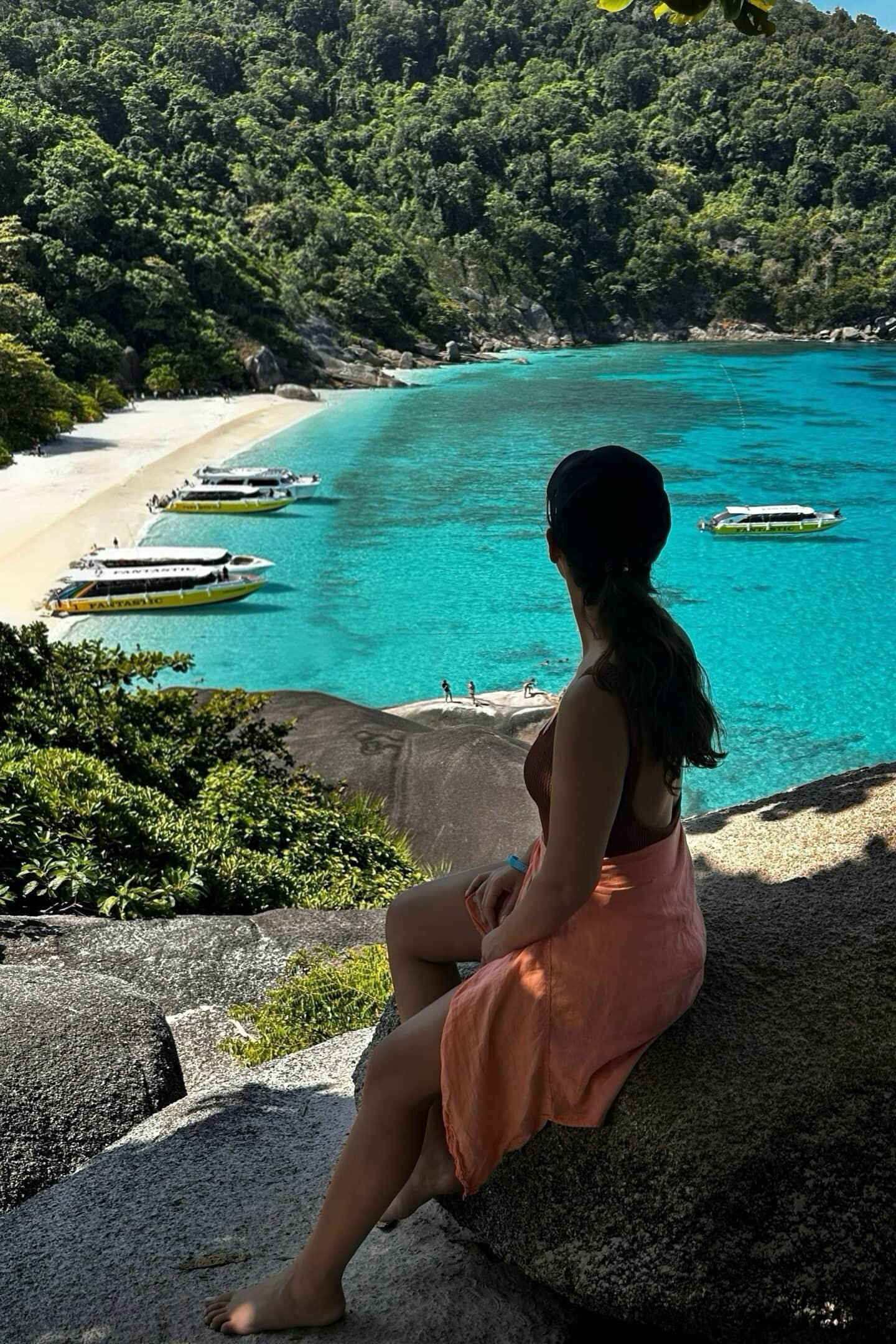 Similan Adaları’nda kayalık noktadan turkuaz koyu izleyen kadın: kıyıda tekneler.