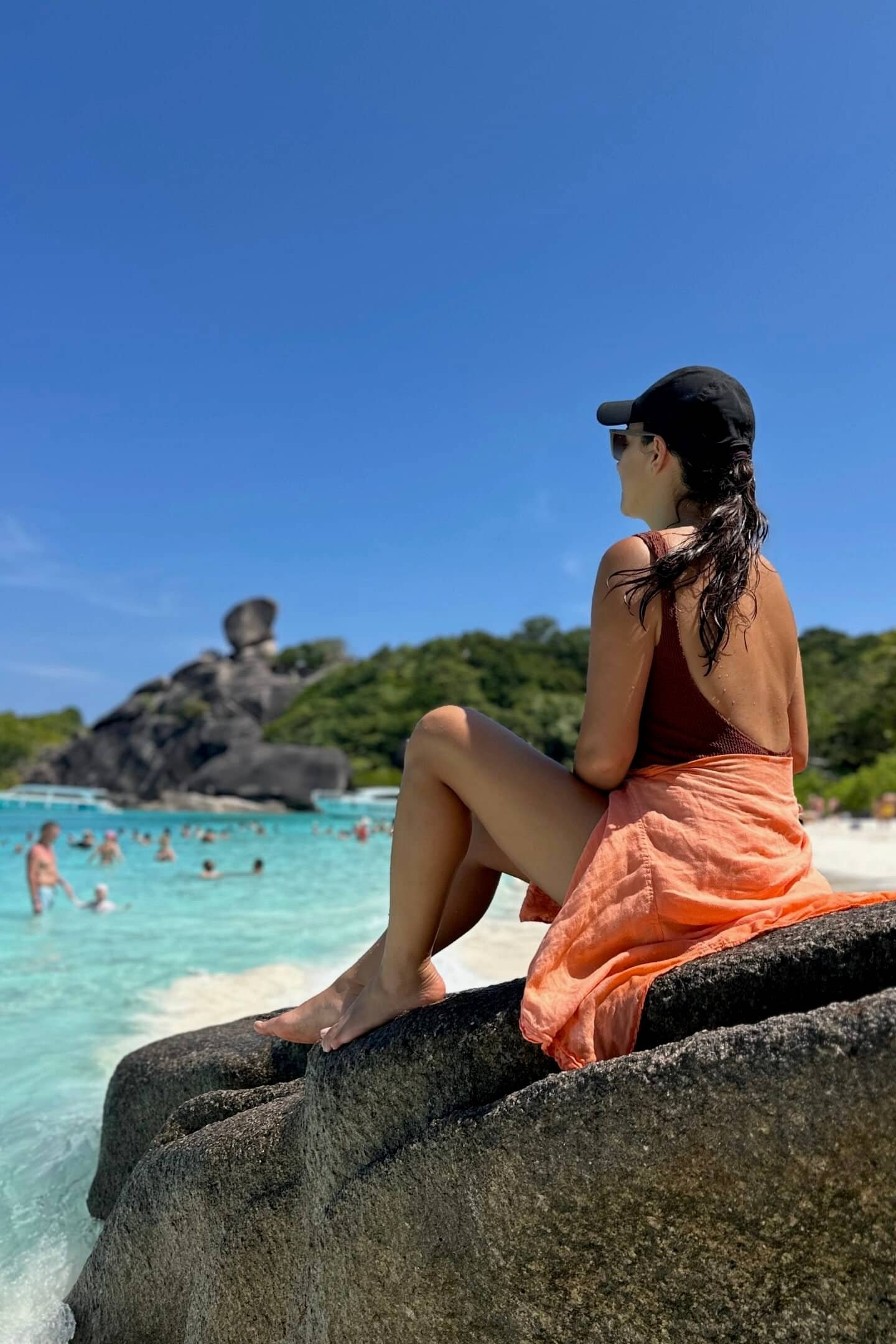 Similan Adaları’nda sahilde kayalık üzerinde oturan kadın, turkuaz deniz ve kumsal.