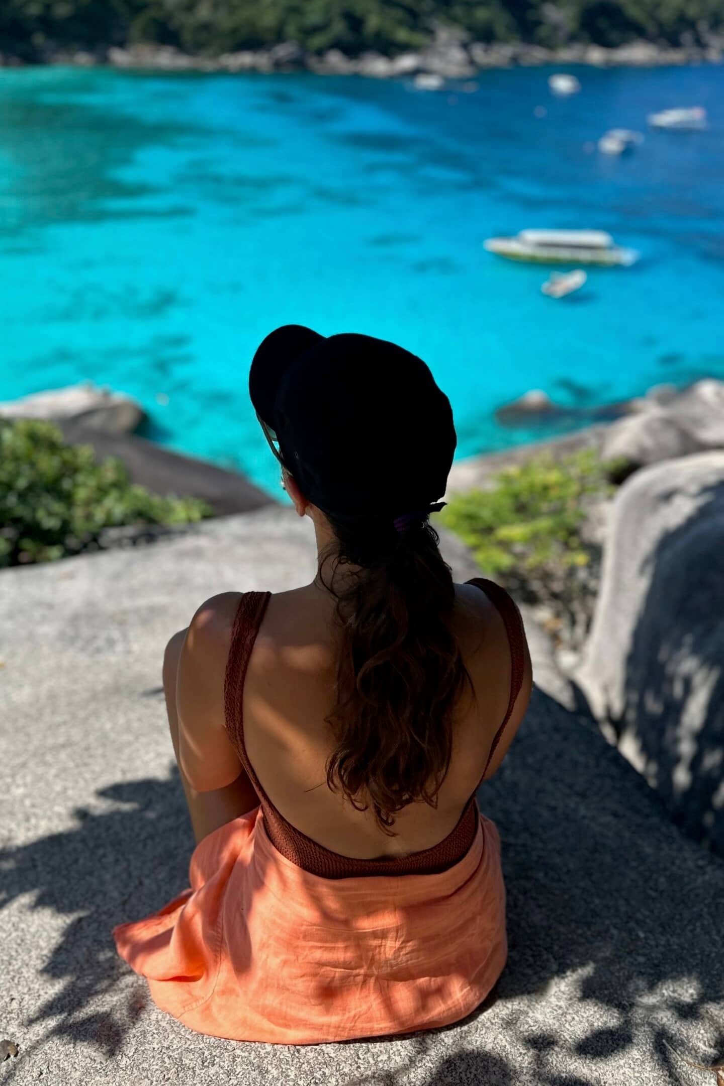 Similan Adaları’nda kayalıkta oturup turkuaz koyu izleyen kadın: kumsal ve tekneler