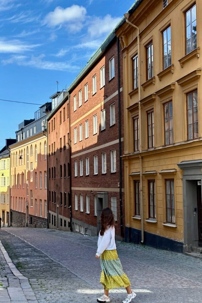 Stockholm Södermalm’de renkli binaların sıralandığı yokuşlu taş sokakta yürüyen kadın
