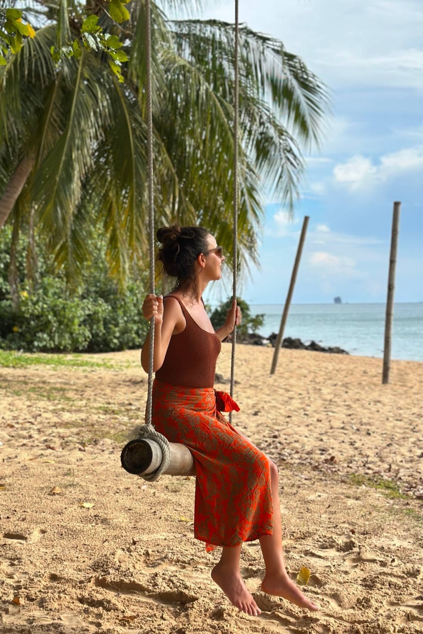 Palmiye ağaçları altında sahilde salıncakta oturan kadın, tropik ada atmosferi