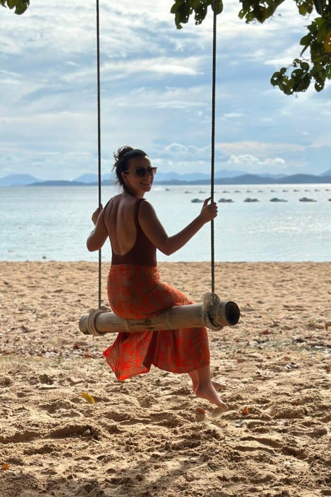 Tayland’da kumsalda denize karşı salıncakta oturan kadın, arkada sakin deniz ve adalar