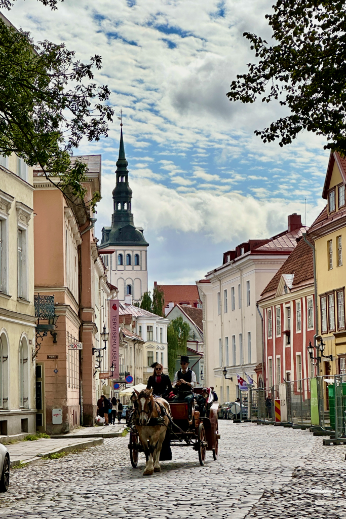 Tallinn Old Town sokaginda atli fayton, renkli binalar ve kilise kulesi.