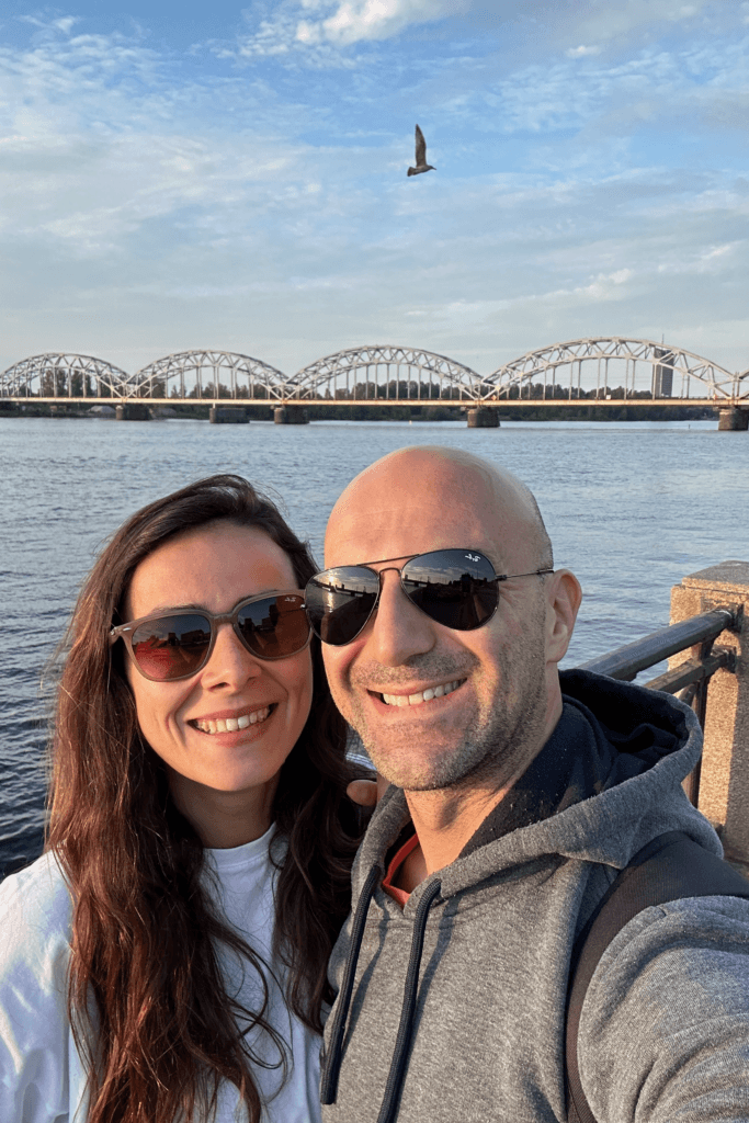 Riga’da Daugava Nehri kıyısında köprü manzarasıyla çekilen çift selfie fotoğrafı